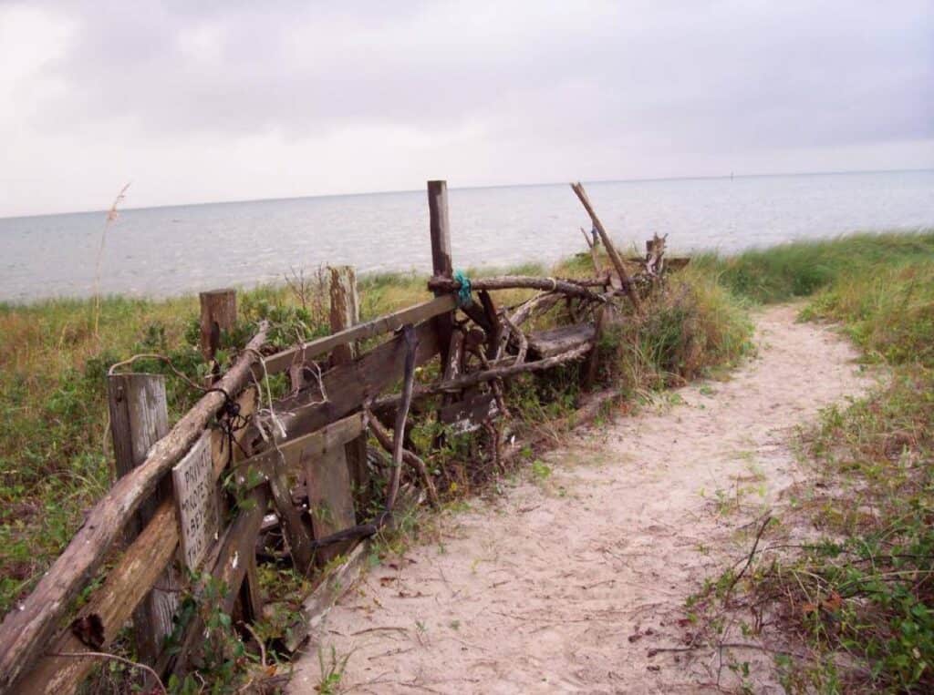 Sandy path to beach with rustic wooden fence.