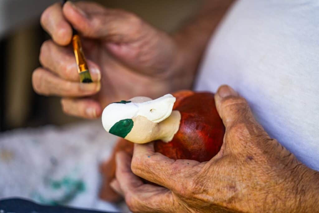 Person painting a wooden duck sculpture