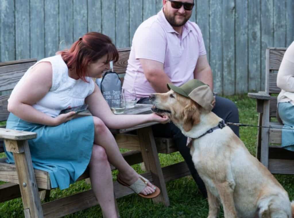 Woman petting dog wearing a hat outdoors.