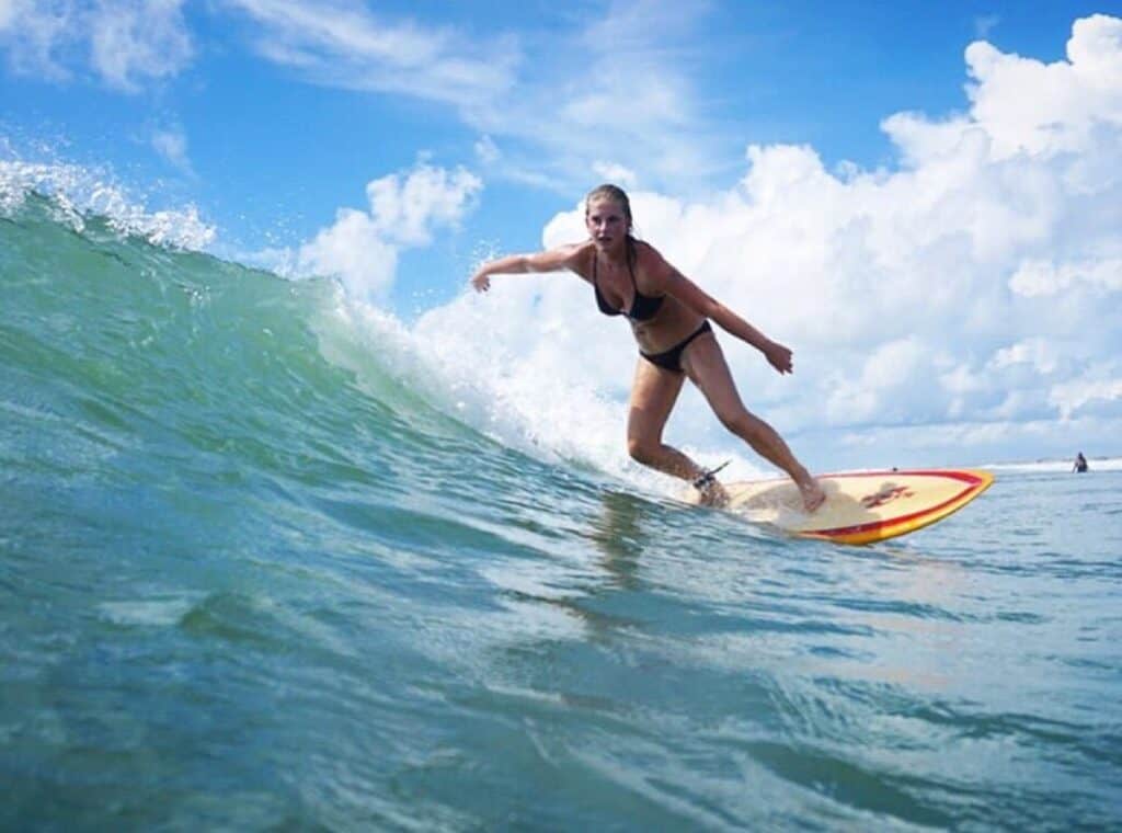 Woman surfing on ocean wave under blue sky.
