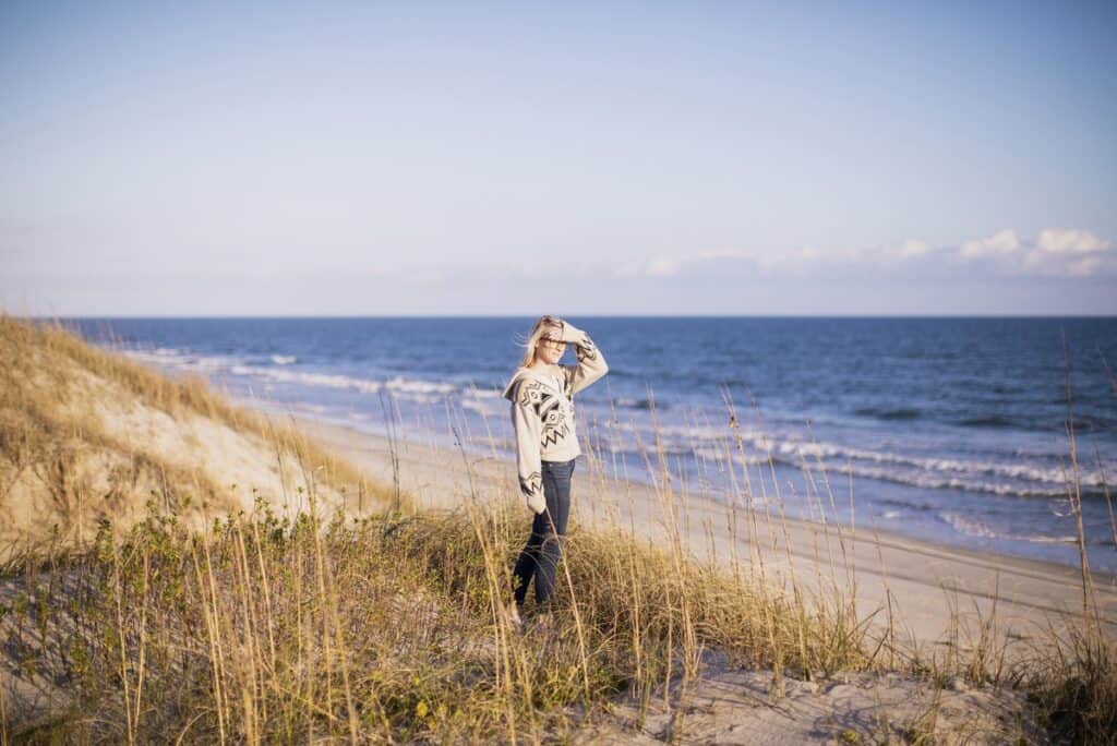 Person standing on beach dune, ocean in background.